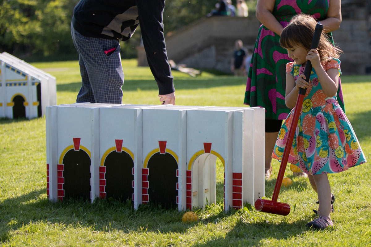 Small child holding a croquet mallet against an architectural croquet hoop