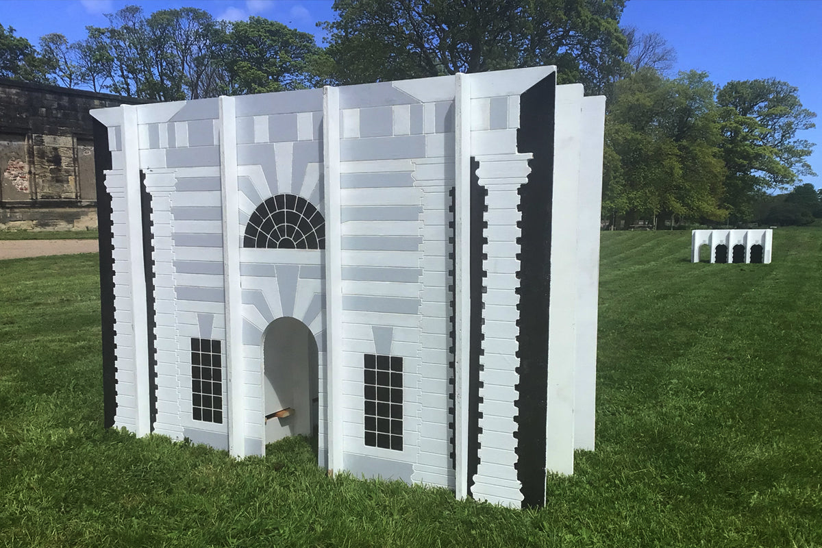 Grey, white and black architectural sculpture in a green landscape.