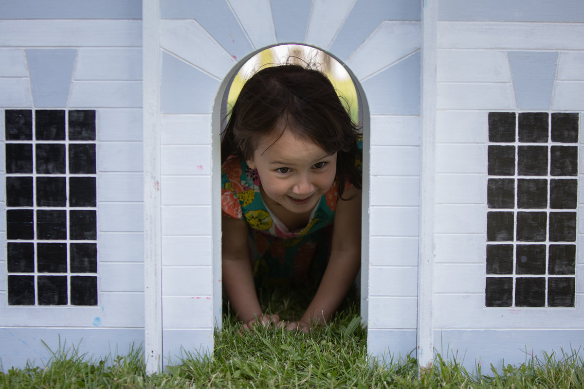 Small child on their hands and knees looking through the doorway of an architectural sculpture