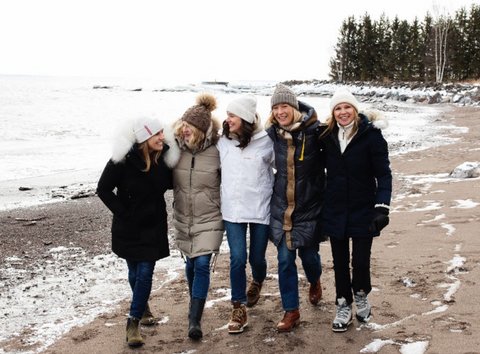 Five women dressed in parkas and winter hats walk along an icy shoreline