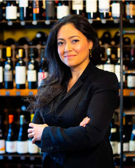 A front facing picture of co-owner of Despaña, Angelica Intriago, with her arms crossed in front of shelves of wine. 