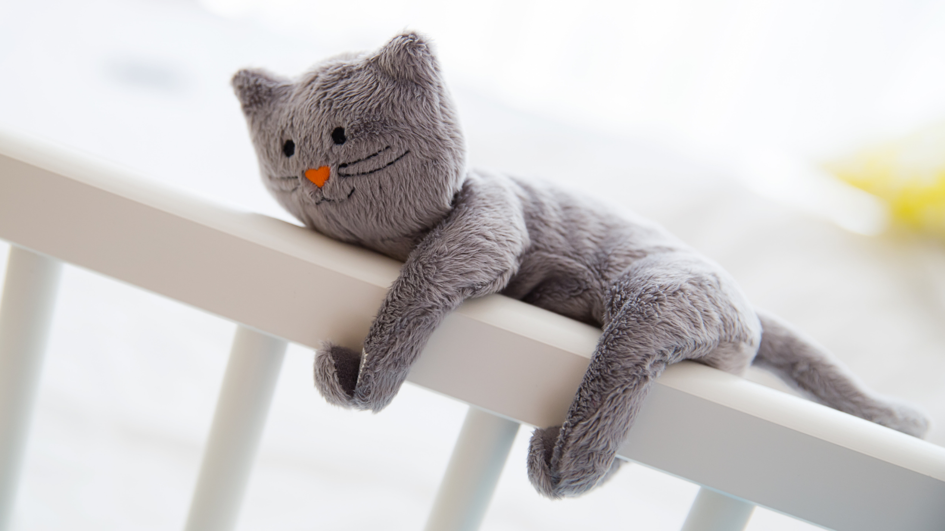Grey, plush cat toy clings to railing of baby crib. 
