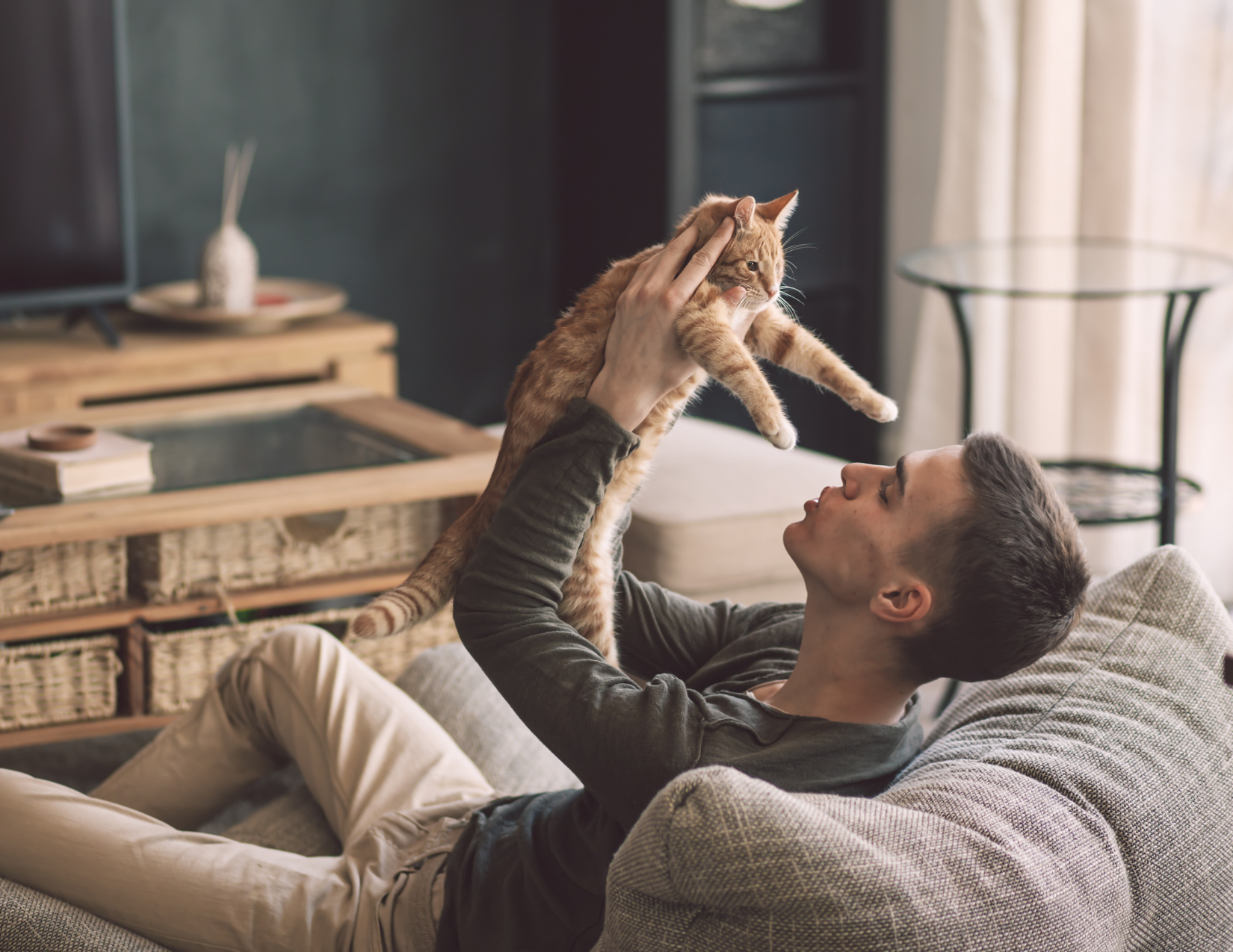 A man holds his cat up in the air lovingly. 