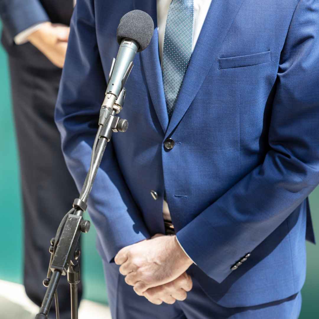 Man in suit talks into a microphone at press briefing.