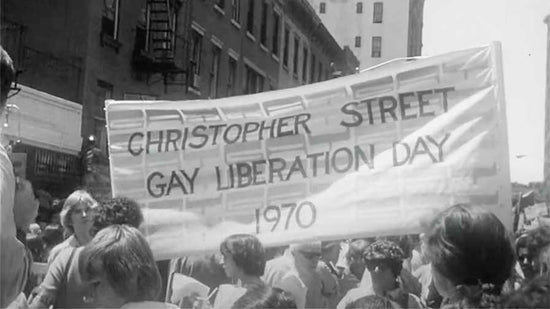 A huge banner reading Christopher Street Gay Liberation Day 1970 is held aloft among a group of people about to set off on the march
