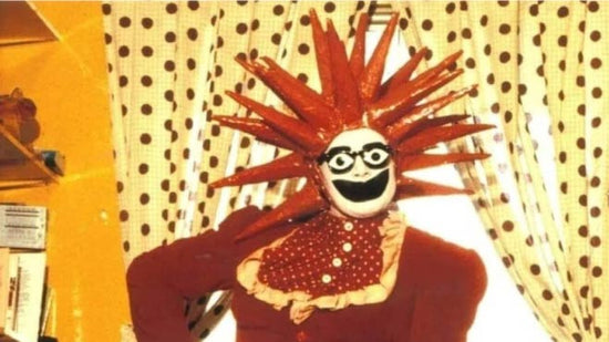 Leigh Bowery in a red spiky plastic hat and white and black face paint
