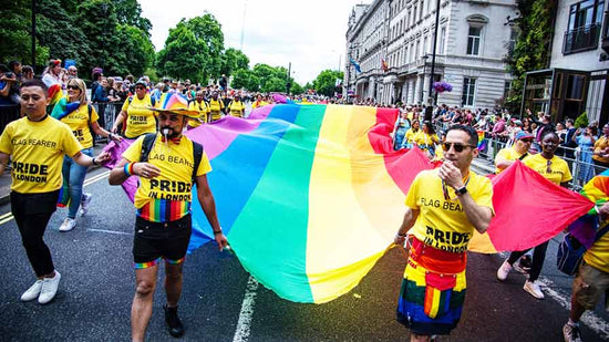 The Pride Parade at Pride In London with about 50 people in matching yellow t-shirts holding a massive Rainbow Pride Flag