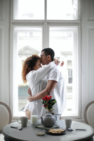 man kissing a woman on the forehead near the breakfast table in the morning