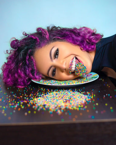 A woman with purple hair posing with sprinkles on her tongue