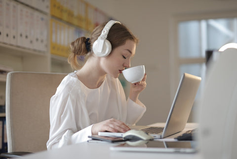 a woman listening to music using white headphones and drinking from a cup while working on her desk