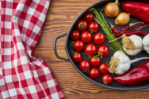 A pan containing cherry tomatoes, chilli, garlic, onion and a red table cloth