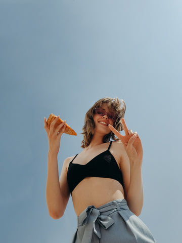 a woman wearing sunglasses, holding a pizza and posing confidently for the camera