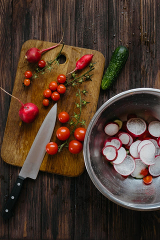 A cutting board with cherry tomatoes, cucumber, radishes and other healthy vegetables