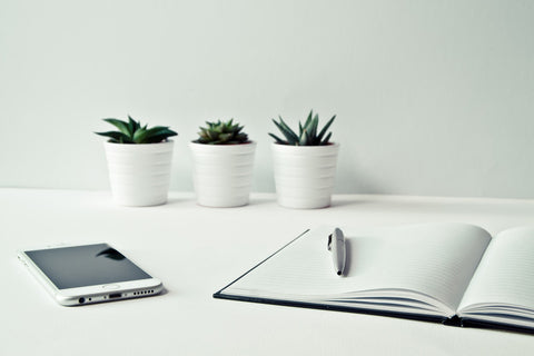 a white desk with three white pots, white phone and a white laptop to make office space productive