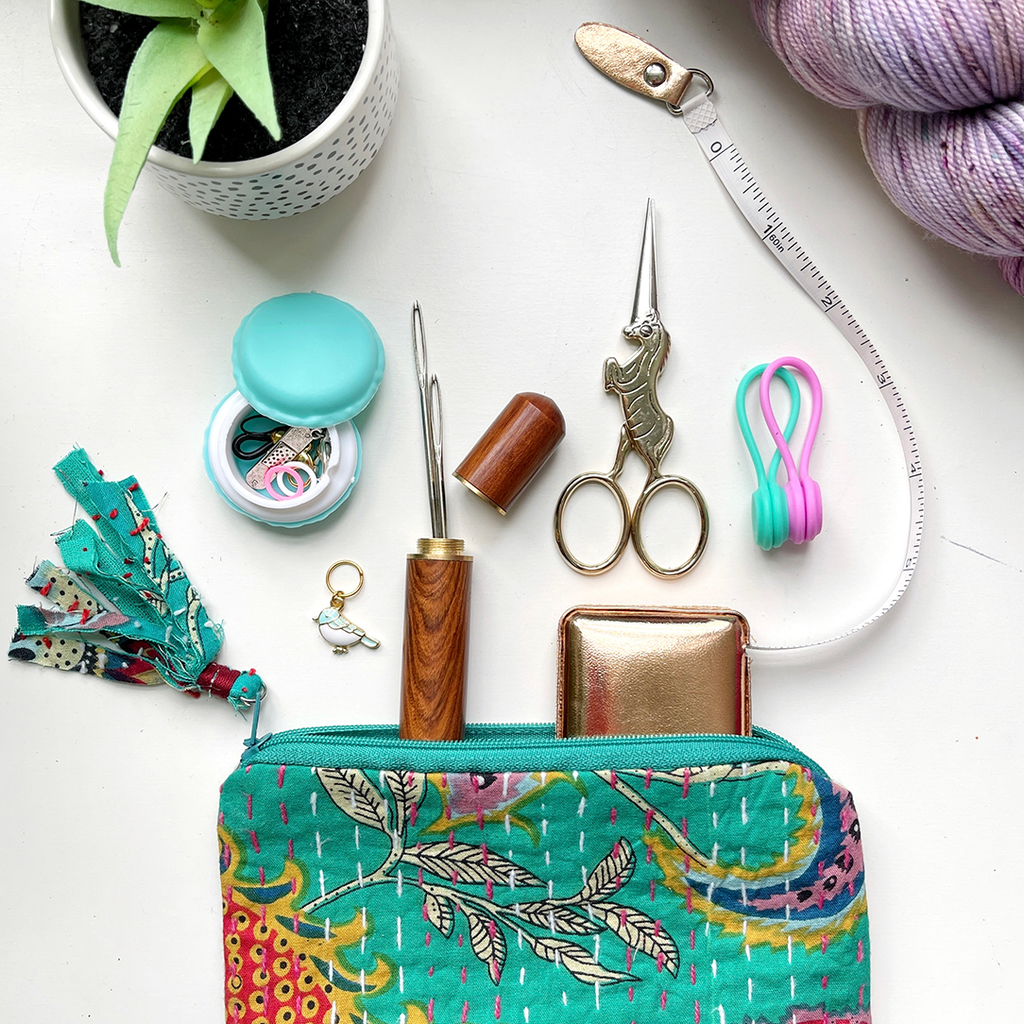 Display of a small notions pouch with basic, must have notions displayed, including stitch markers, scissors, darning needle, and tape measure