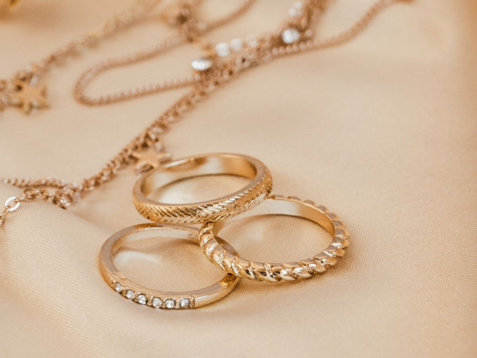 Gold rings and necklace on a beige fabric background