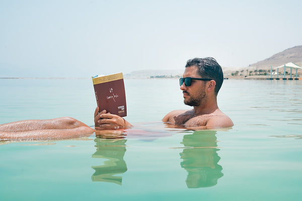 a man with a thick beard reading a book at the beach
