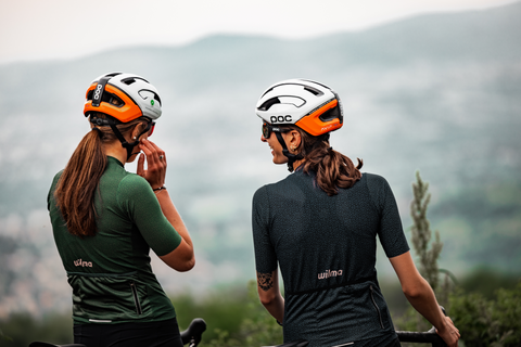 Deux femmes faisant une pause dans leur sortie à vélo. Elles rigolent face à l'horizon. Elles sont habillées avec des jerseys de cyclisme de la marque de vêtements Wilma.