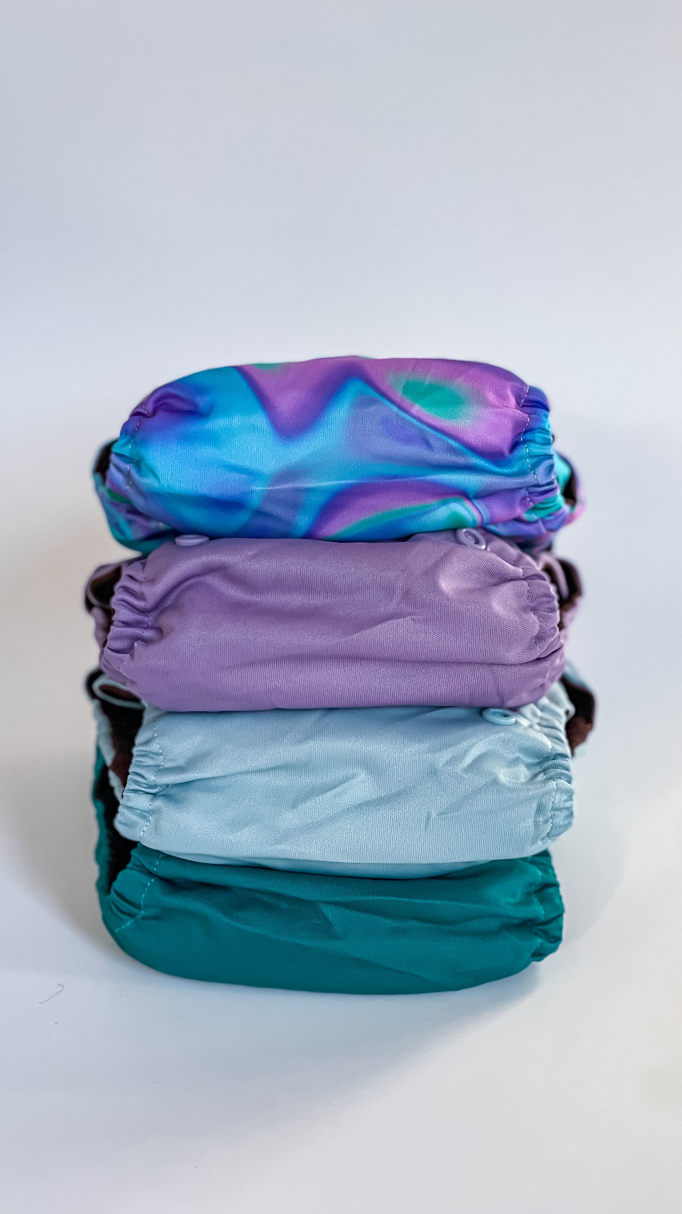 Stack of Jubel reusable nappies in colours Nordlicht, lilac, duck egg, and teal