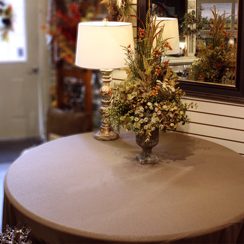 empty table with tan tablecloth, a small lamp and a fall floral arrangement
