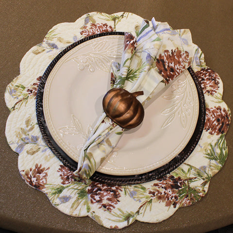 a fan folded napkin in a copper pumpkin napkin ring, on top of a white ceramic plate, on top of a dark brown charger plate, on top of a floral placemat, on top of a tan tablecloth