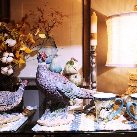 pheasants on a shelf with striped placemats, a framed photo of flowers, an arrangement of cotton, and a lit lamp