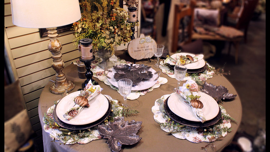set dinner table, with three place settings and a floral center piece.  white dishes and serving tray with dark gray maple leaf shaped salad dishes.  each place setting has a folded napkin inside of a copper pumpkin napkin ring, on top of a white ceramic plate, dark brown charger plate, floral ring coordinating with the centerpiece and placemat.
