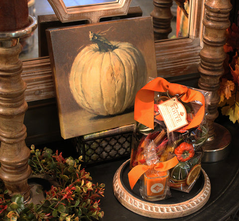 a small canvas with a white pumpkin print behind a bag of potpourri with an orange bow