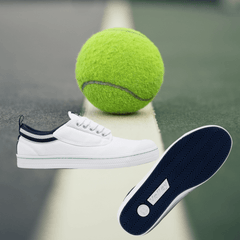 A pair of white dunlop volleys on a tennis court with a tennis ball.