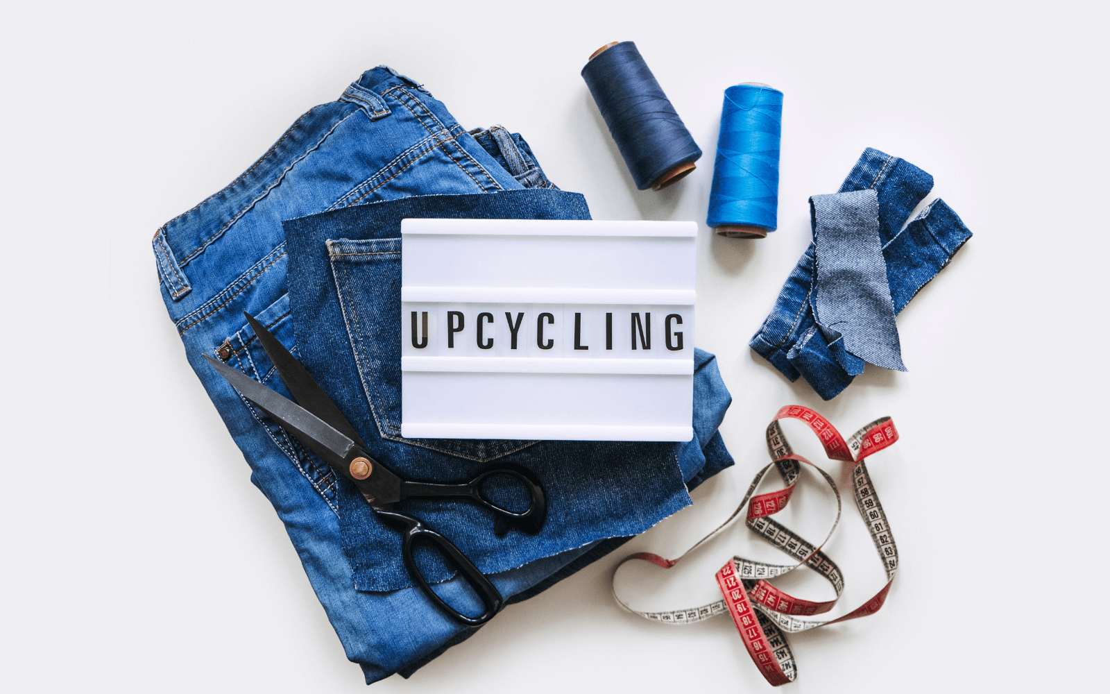 Sustainable fashion. Repurpose, recycle or donate. A photo of some jeans with sewing equipment and a sign that says Upcycling.