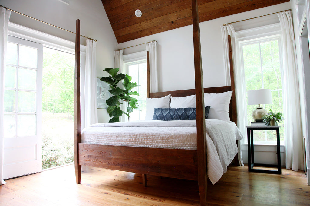 A dark wood tall four-poster bed in a bedroom with white linen drapes and curtains