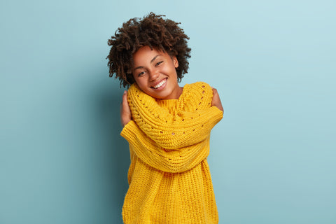 A happy model wraps her arms around herself in an act of self love and acceptance.