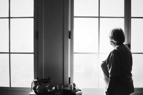 A black and white photo of a lady looking out of a window.