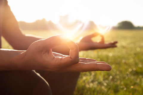 Individual with their hands in an yoga pose sitting outside.