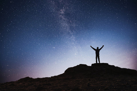 Man on the top of a mountain lifting his arms high in the air.