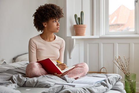 Young woman looks out the window as she writes in her journal