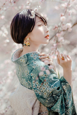 満開の桜の下でお花見を楽しんでいる明るい緑色の着物を着た美しい日本人女性