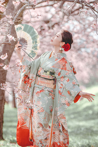 満開の桜並木を眺める扇子を持った美しい着物の女性