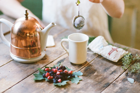 a Piper and Leaf tea ball dripping over a cup of seasonal tea surrounded by fun festive christmas decor 