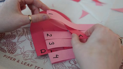 Piper and Leaf crafter weaving papers together with according letters and numbers for a DIY valentine galentine craft