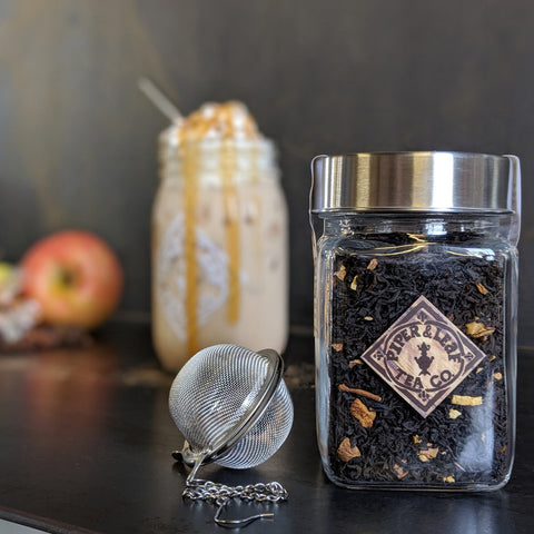 A loose leaf jar of Caramel Apple Pie and a tea ball. Further back is a jar of tea dripping with caramel drizzle.