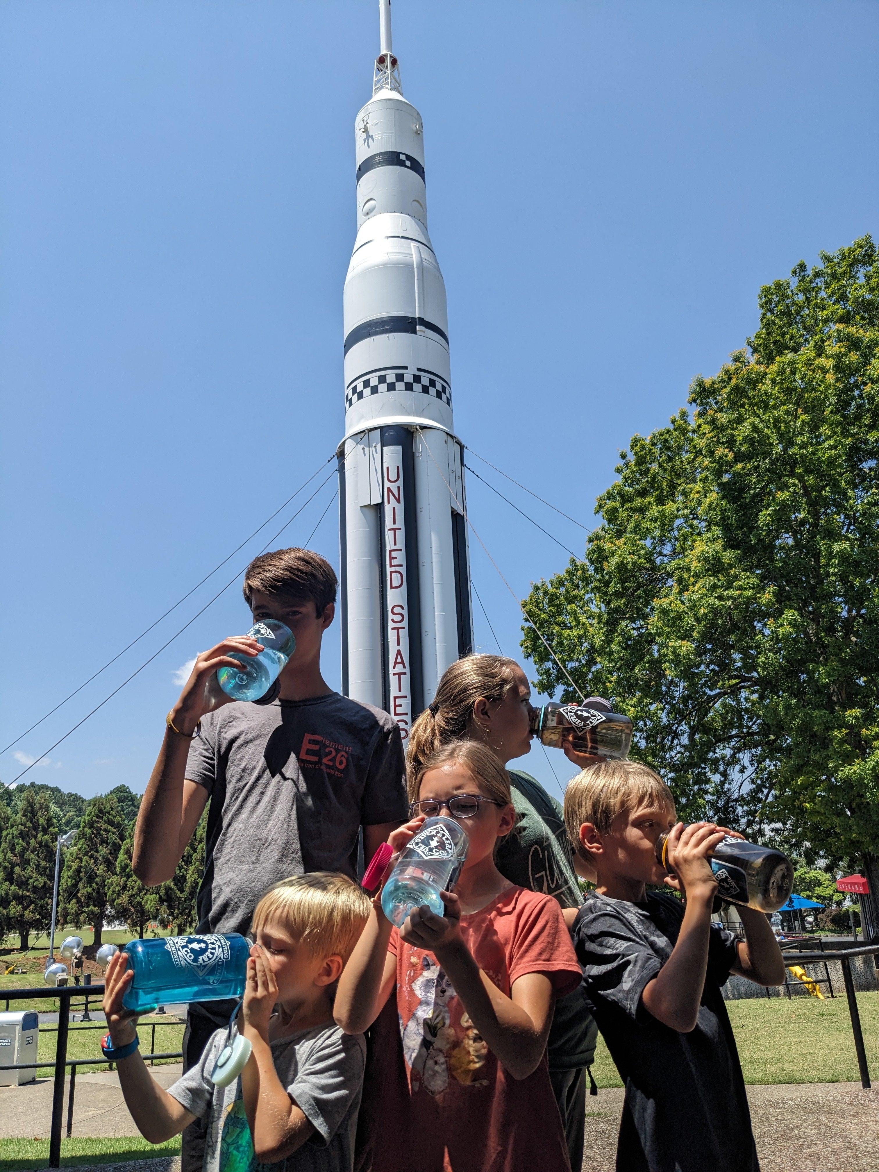 5 of the Christopher kids, drinking water out of their nalgenes in front of Huntsville's very own Saturn V, at the United States Space and Rocket Center