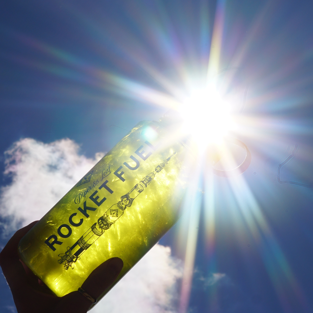 Lime Green Piper and Leaf Rocket Fuel Nalgene held to the sky, illuminated by the radiant beams of sun