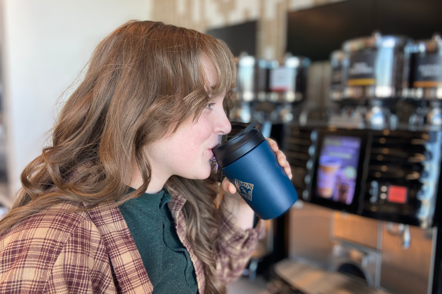 A girl drinking out of an insulated travel mug inside a gas station