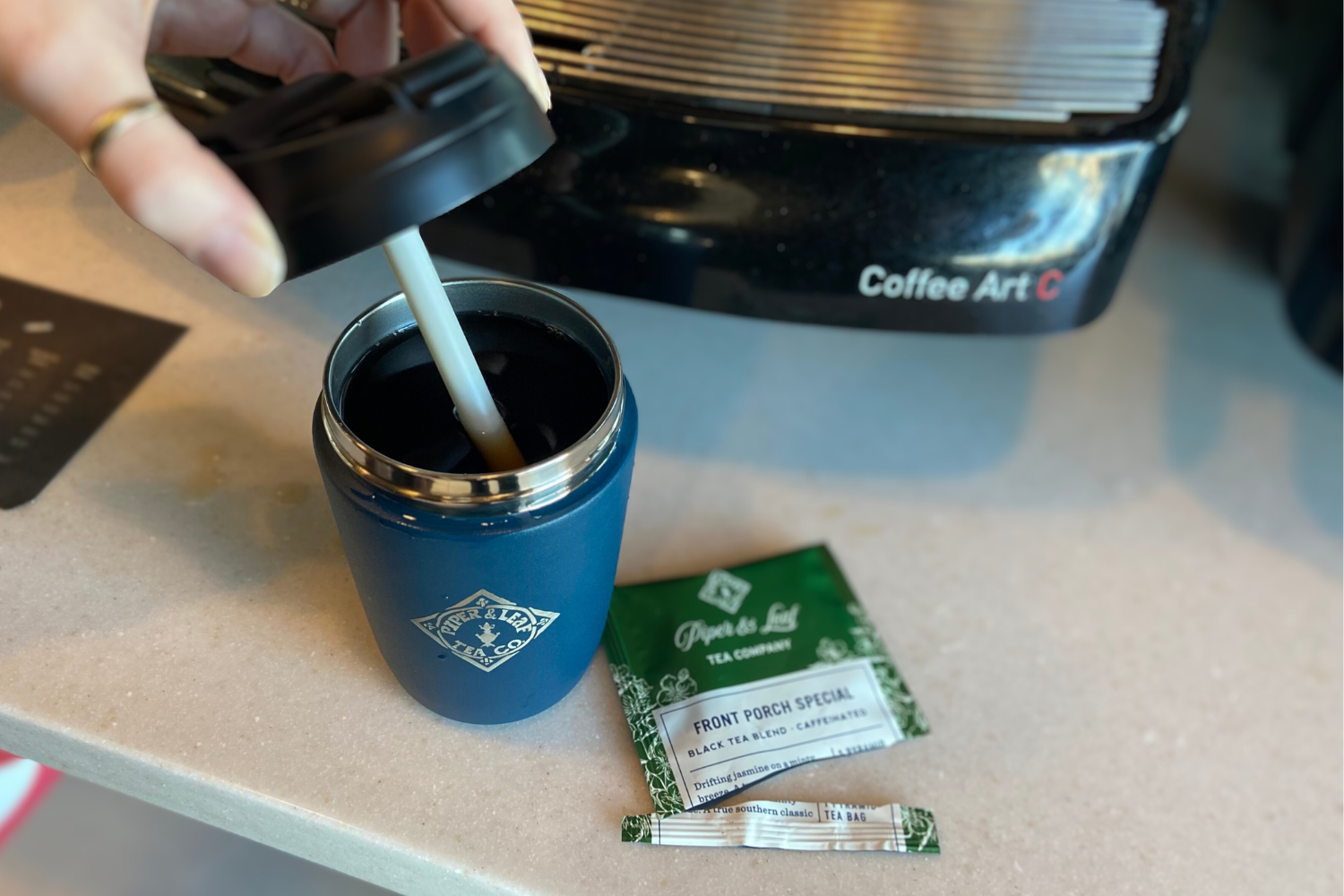 A lid being put on an insulated travel mug with an open individually wrapped tea bag next to it, inside a gas station