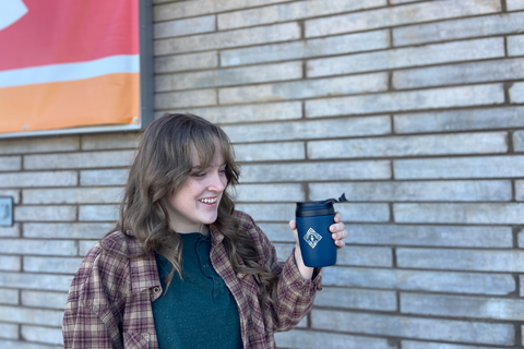 A happy girl holding a Piper and Leaf Super Sippy in front of a brick wall