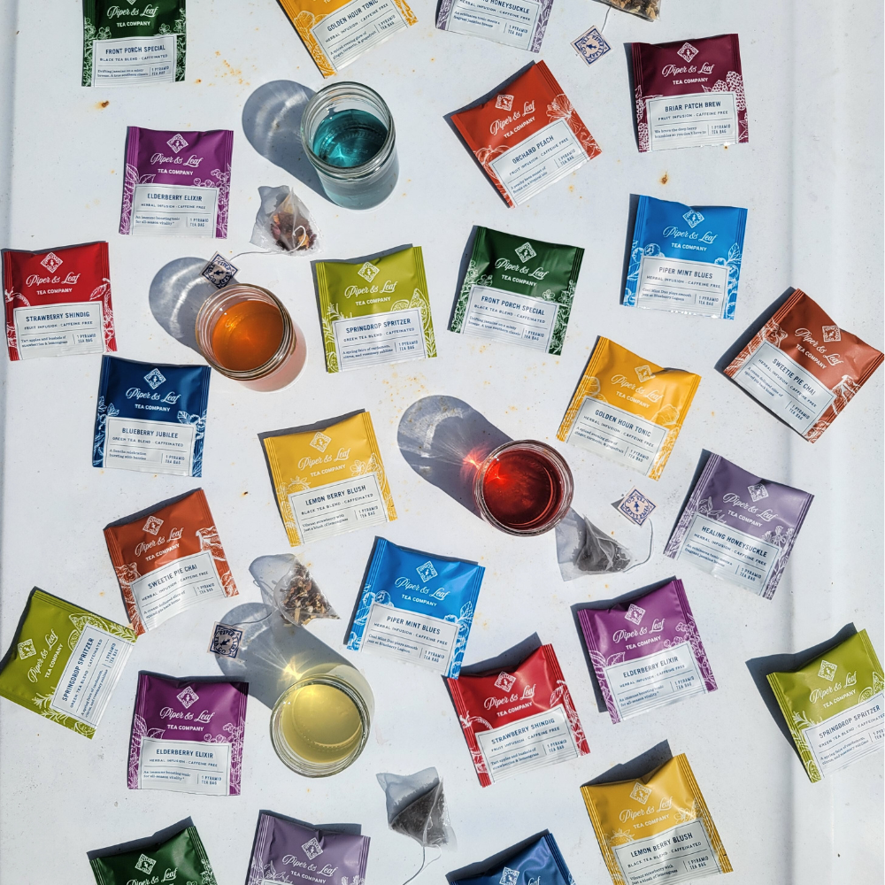 A variety of individually wrapped tea bags with small cups of tea spread over a white surface