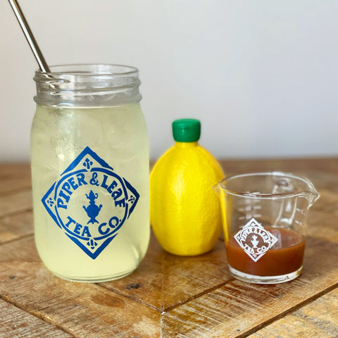 A pint jar of lemonade, lemon, and tiny measuring cup of tea concentrate