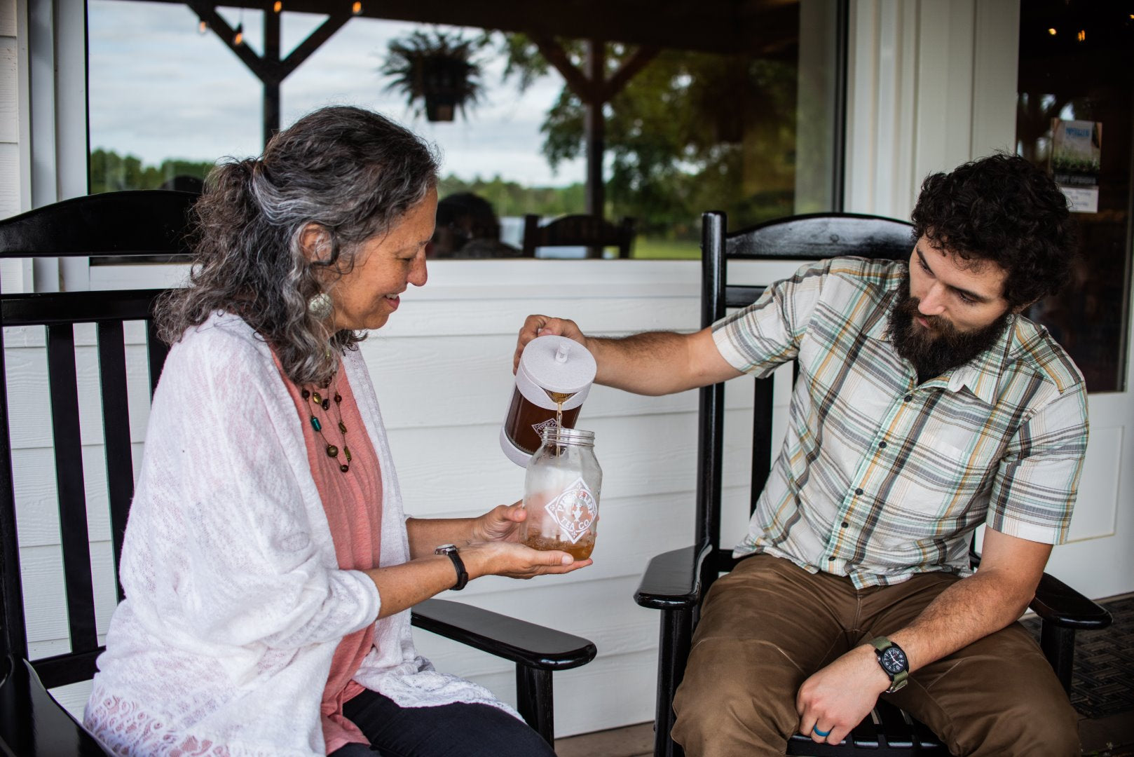 A son pouring his mom a jar of freshly brewed Piper and Leaf tea into a empty Piper and Leaf quart jar.