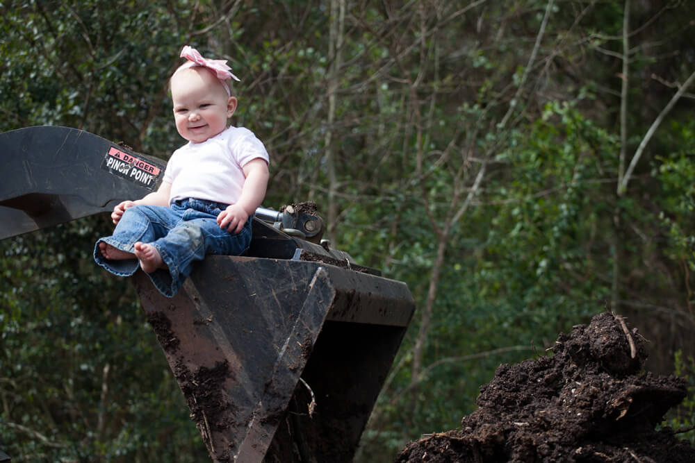 A baby with a bow on sitting on top of an excavator